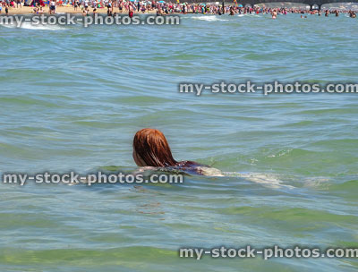 Stock image of sunny beach with girl swimming in sea, doing breaststroke