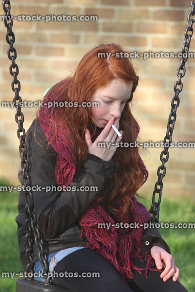 Stock image of young teenage girl smoking underage / youth sitting on playground swing