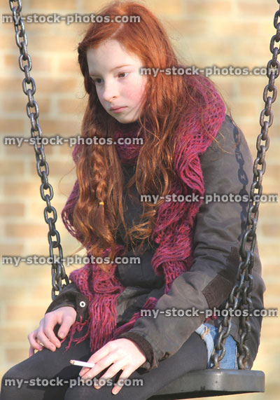 Stock image of young teenage girl smoking underage / youth sitting on playground swing