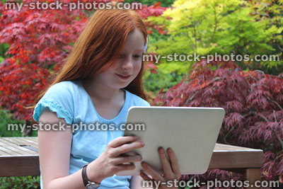 Stock image of young girl reading tablet computer / iPad in garden