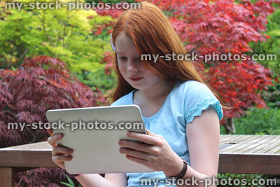 Stock image of young girl reading tablet computer / iPad in garden