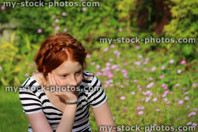 Stock image of young girl daydreaming in summer garden, resting head on hand