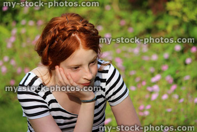 Stock image of young girl daydreaming in summer garden, resting head on hand
