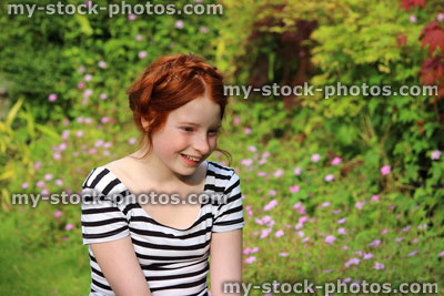 Stock image of happy young girl sitting / smiling in summer garden, looking down