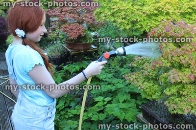 Stock image of young girl watering garden bonsai trees with hose