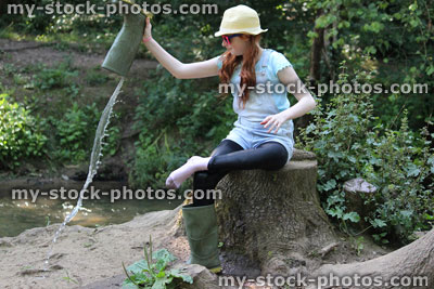 Stock image of girl by river, pouring water out wellie boots