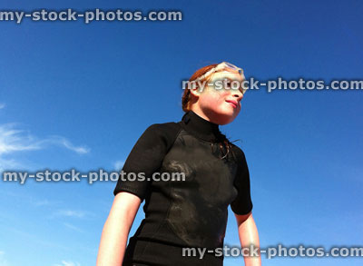 Stock image of young girl wearing a wetsuit at beach, with blue sky
