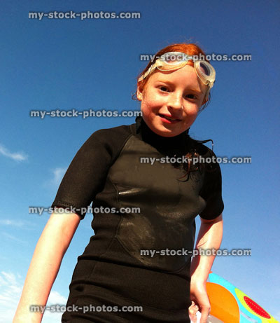 Stock image of young girl wearing a wetsuit at beach, with blue sky