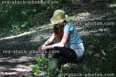 Stock image of girl in woodland forest, straw hat, looking at floor, sitting on log