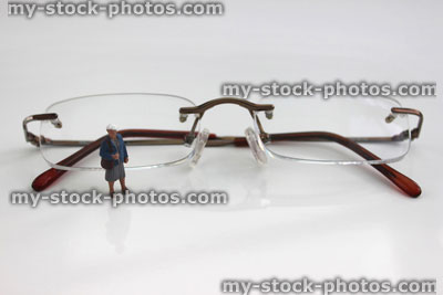 Stock image of mini people stood by lenses of designer, frameless spectacles