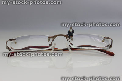 Stock image of mini people stood by lenses of designer, frameless spectacles