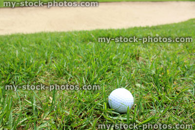 Stock image of golf ball in grass on golf course, sandy bunker (close up)
