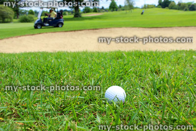 Stock image of golf ball in grass, with golf buggy and sandy bunker