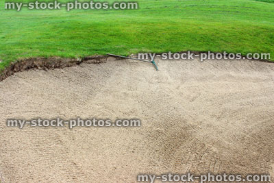 Stock image of freshly raked sandy bunker trap at golf course, with rake