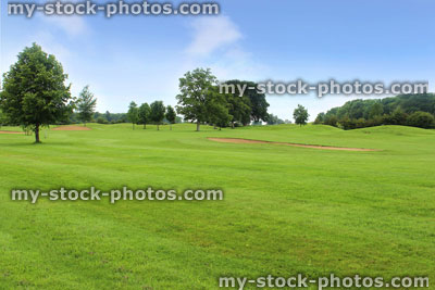 Stock image of golf course with green grass, trees, sandy bunker traps, sky