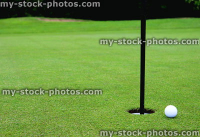 Stock image of golf ball by hole and flag, putting green, golf course