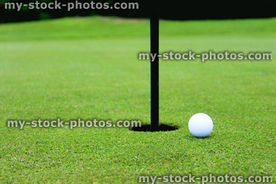 Stock image of golf ball by hole and flag, putting green, golf course