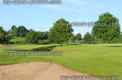 Stock image of golf course with sandy bunker trap, trees, rough and fairways
