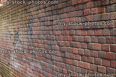 Stock image of red brick wall in sunshine, graffiti writing spray painted