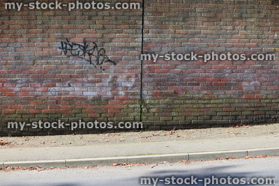 Stock image of dirty red brick wall with graffiti tags, green lichen