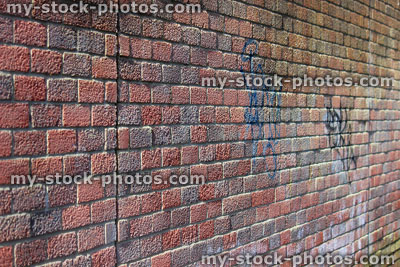 Stock image of sunny red brick wall, with graffiti and textured surface