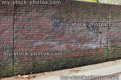 Stock image of dirty red brick wall, spray painted graffiti tags, run down area