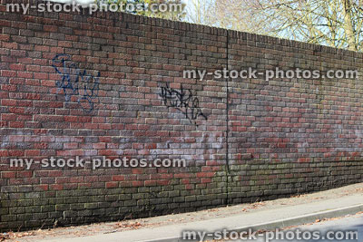 Stock image of red brick wall next to road / pavement, graffiti