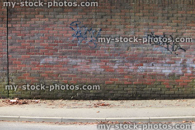 Stock image of red brick wall, graffiti writing tags, tarmac pavement