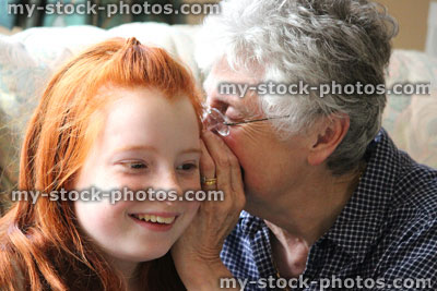 Stock image of grandmother whispering secret in young granddaughter's ear, listening