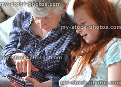 Stock image of girl showing grandmother how to use mobile phone / smartphone