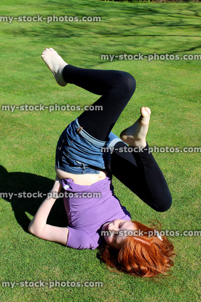 Stock image of red haired girl exercising and stretching on a manicured lawn