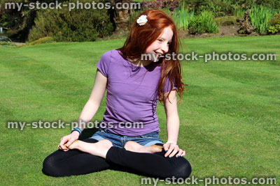 Stock image of red haired girl posing in lotus position on manicured lawn