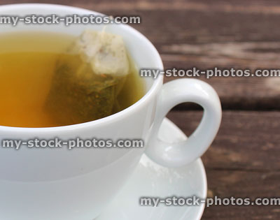 Stock image of cup of green tea, white cup, saucer, teabag
