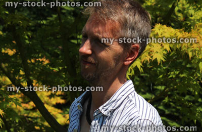 Stock image of man standing in sunny garden, enjoying strong sunshine