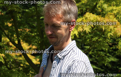 Stock image of man standing in sunny garden, looking downwards, sunshine