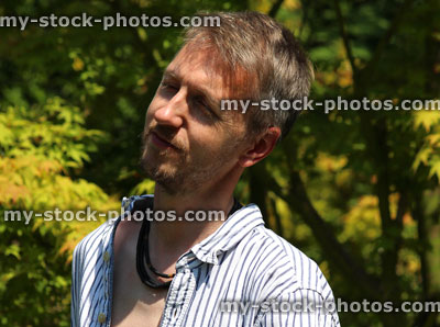 Stock image of man standing in garden sunshine, looking upwards, squinting