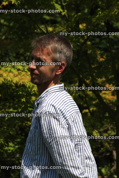 Stock image of man standing in sunny garden, with hands behind back