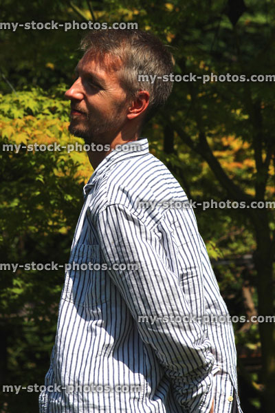 Stock image of man standing in sunny garden, with hands behind back