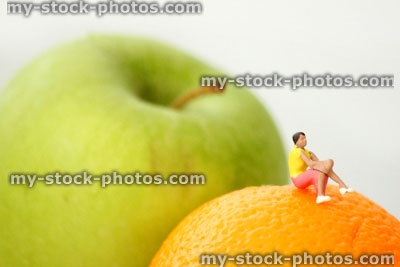 Stock image of healthy eating concept, with mini person sat on fruit