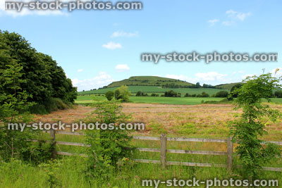 Stock image of steep hill in countryside, with wooden fence, fields