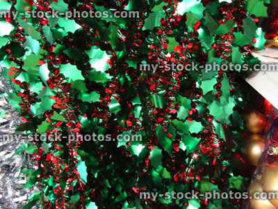 Stock image of coloured tinsel Christmas decorations, sparkling green holly leaves, red berries garland