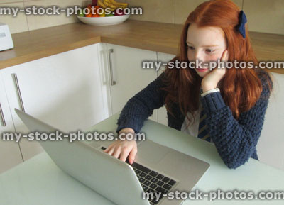 Stock image of girl doing homework on laptop, at kitchen table