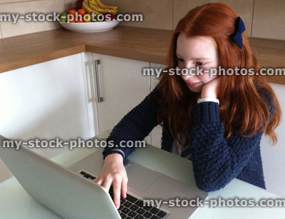 Stock image of young girl with laptop, doing homework on kitchen table