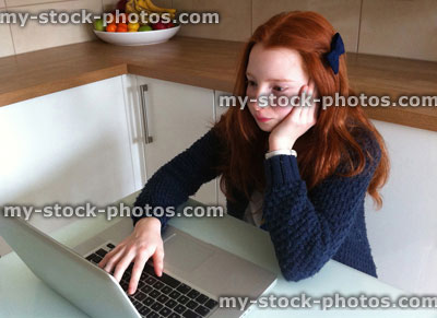 Stock image of girl doing homework on a laptop computer in kitchen