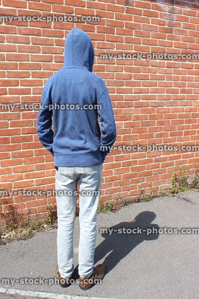 Stock image of teenage boy / youth wearing hoodie, beside brick wall
