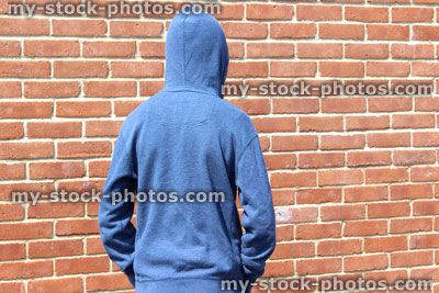 Stock image of teenage boy / youth wearing hoodie, beside brick wall