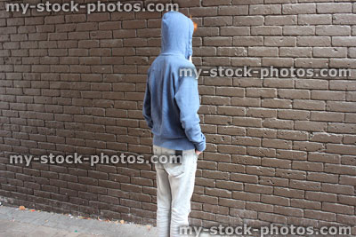 Stock image of teenage boy / youth wearing hoodie, brown brick wall