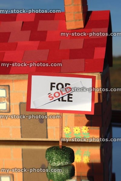 Stock image of cardboard model house, For Sale / Sold sign, reflecting mirror, real estate agent