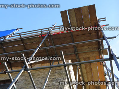 Stock image of stone house with scaffolding poles / planks, repairing roof