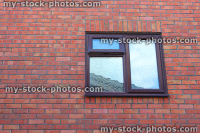 Stock image of brown UPVC bathroom window with frosted glass, red brick house